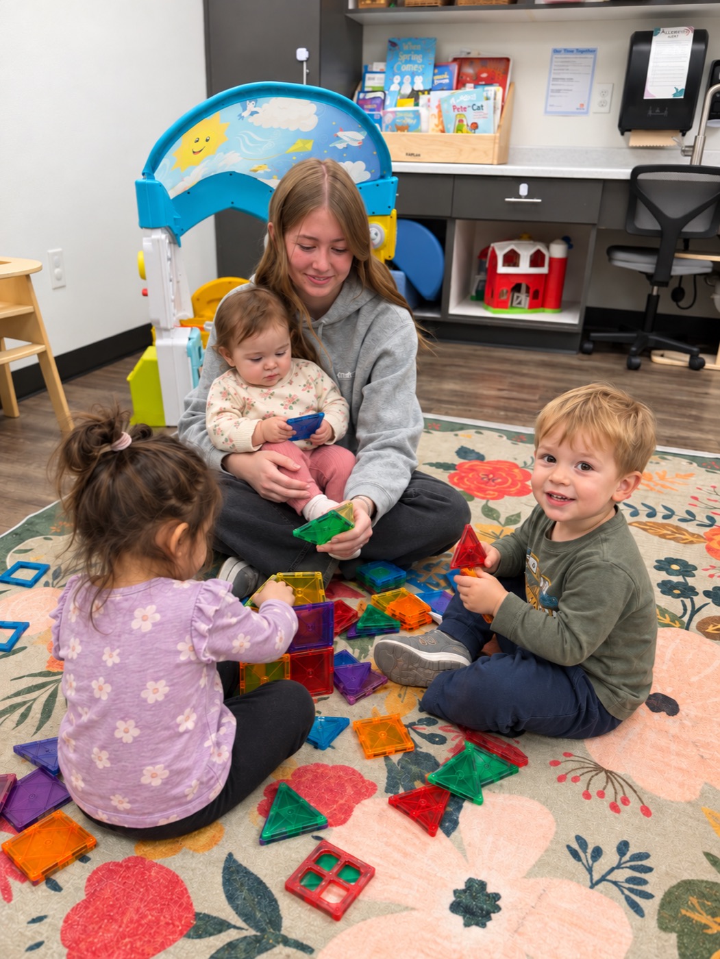 A teacher playing with toddlers on the rug